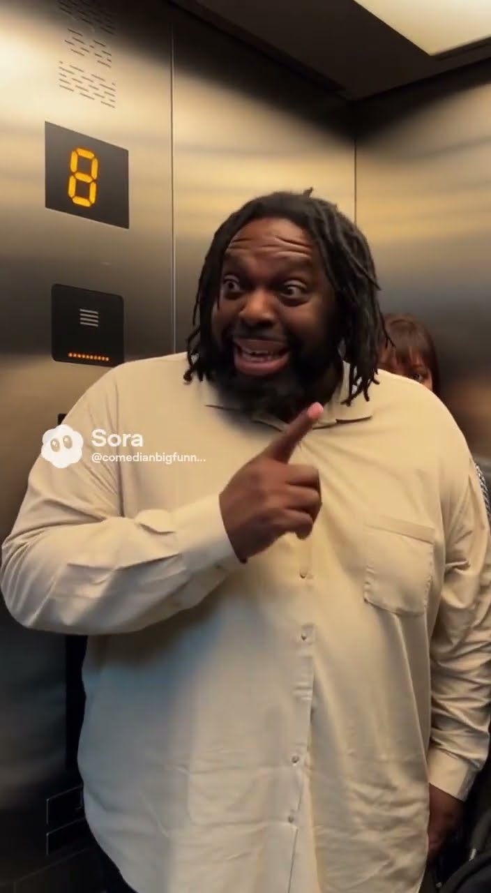 BIG Funny in a cream shirt grinning and pointing over his shoulder inside an elevator stopped at floor 8.